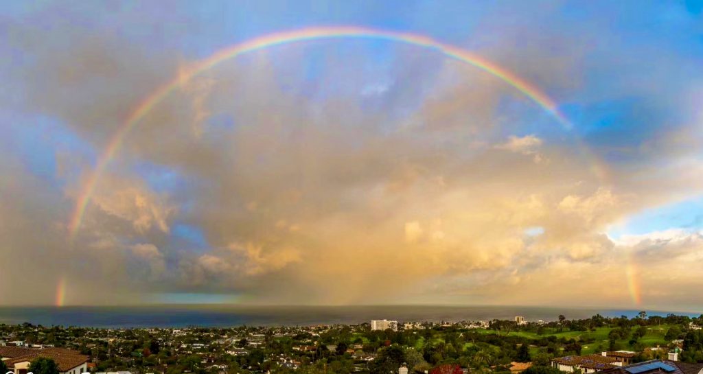 Rainbow over cityscape and ocean under clouds.
