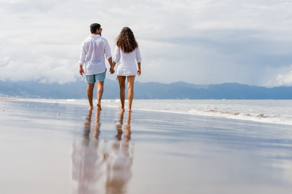 Couple walking on a beach, holding hands.