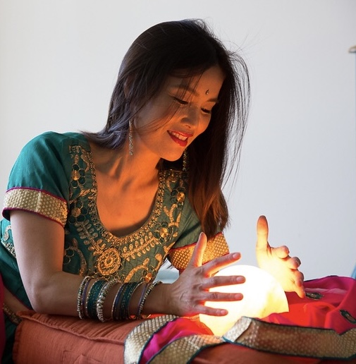 Woman in traditional attire holding a glowing orb, smiling warmly.